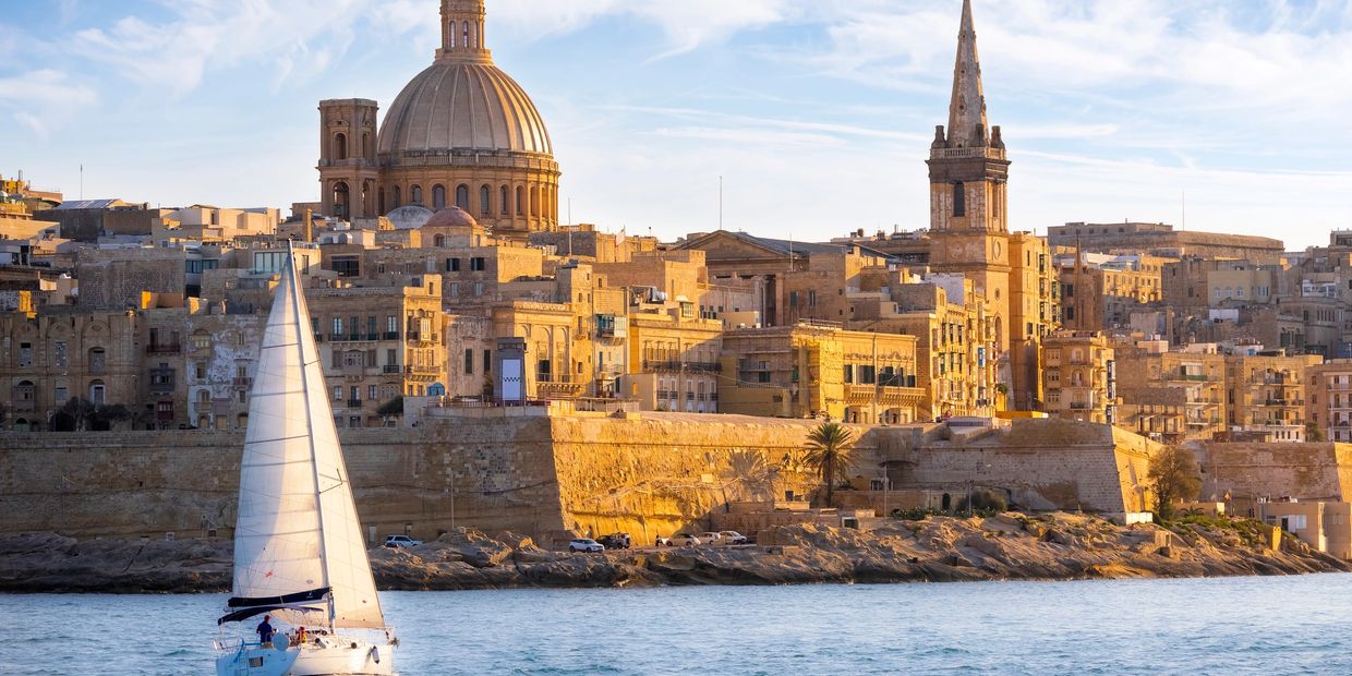 Sailboat near historic city at sunset.