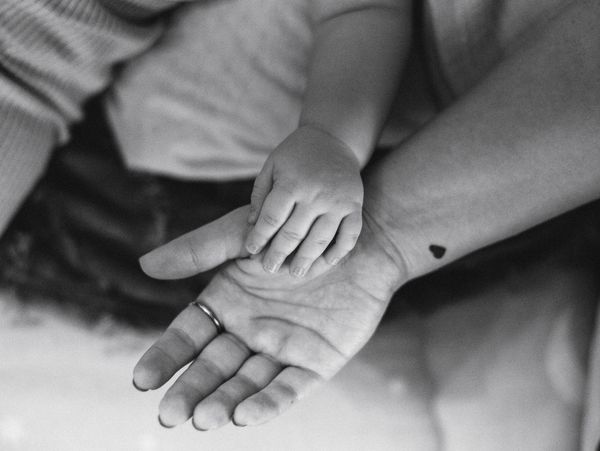 A baby's hand resting on an adult's open palm in black and white.