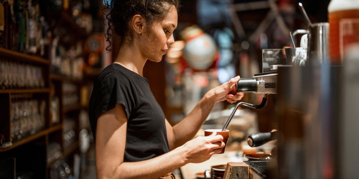 Barista preparing coffee using an espresso machine in a cozy café.