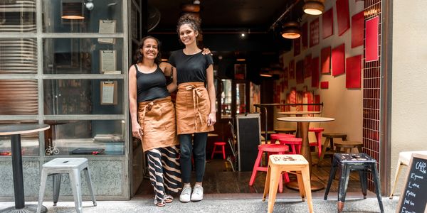 Two smiling cafe staff members standing at the entrance of a cozy cafe.