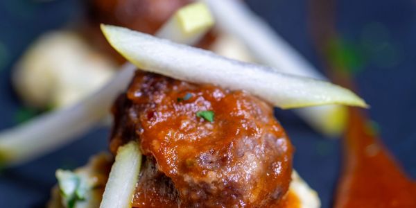 Close-up of a meatball with tomato sauce and sliced pear on top.