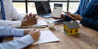 People discussing real estate investment with documents and calculator.