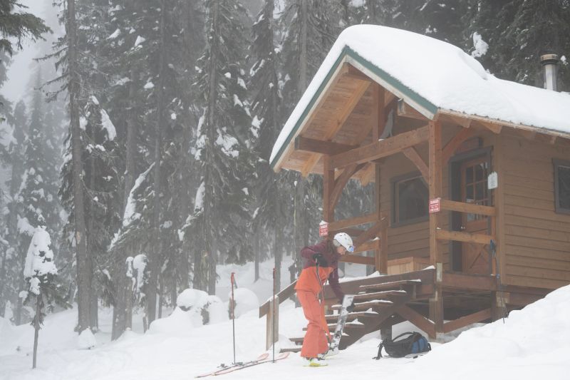 Backcountry skier prepares skis in front of public cabin, Kootenays , B.C.