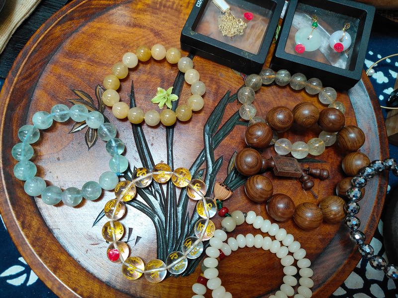 A wooden tray with a variety of bracelets and necklaces on it. The bracelets are made of different materials and have different designs