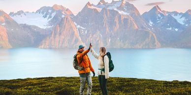 A couple high-fiving in lush green grass in front of mountains and a lake