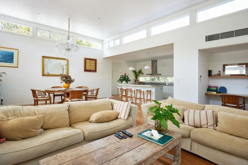 Unoccupied open plan living area with sofas and coffee table, dining table seating four, and kitchen with island and bar stools.