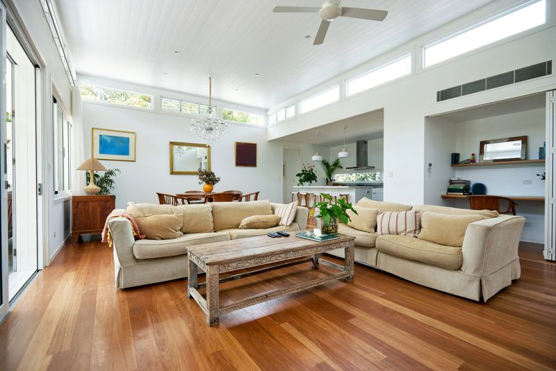 View across living area with sofas and table, dining table and kitchen in background, hardwood floor, ceiling fan overhead.