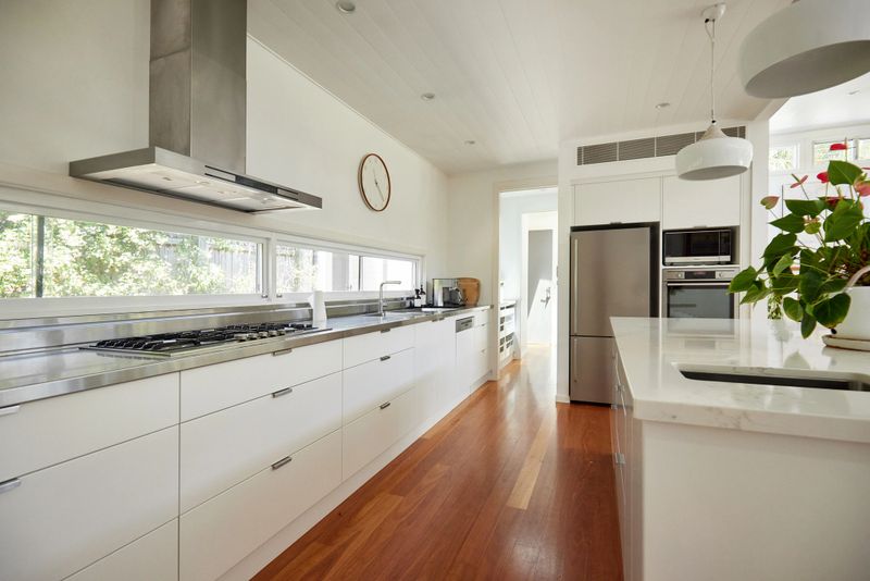 Island, long counter, sink, major appliances, wall clock, pendant lights, and hardwood floor.