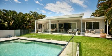 Modern house with a pool and glass fence under a blue sky.
