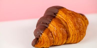 Chocolate-dipped croissant on a white surface with a pink background.