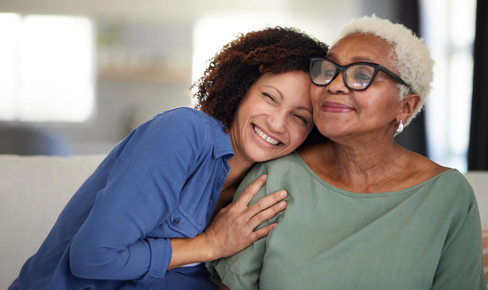 A younger woman affectionately hugging an older woman, both smiling warmly.