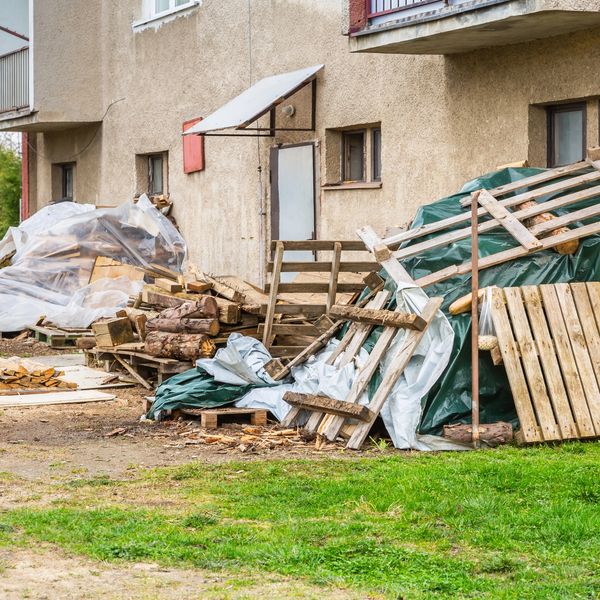 Stacked wooden pallets and logs outside a building.
