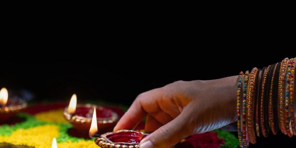 Hand lighting traditional oil lamps on a colorful rangoli.