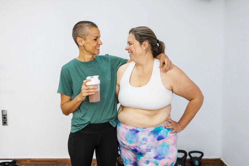Female personal trainer comforting her client and offering her a protein shake after a workout session