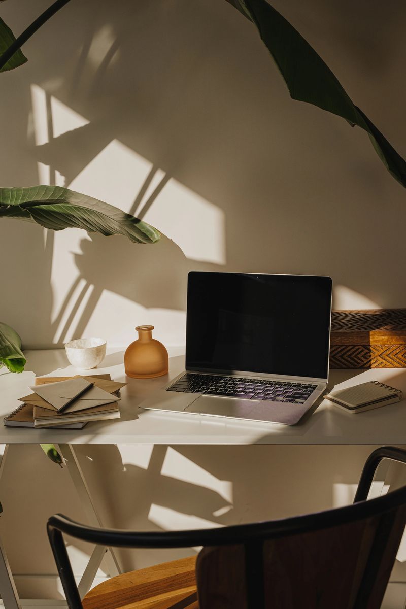 Simple and elegant workspace featuring laptop, notebooks and greenery in a well-lit corner