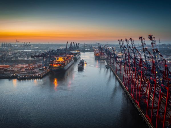 A busy shipping port at sunset with cranes and cargo ships.