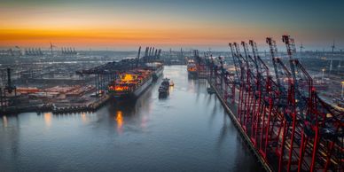 A large industrial port at sunset with cranes and ships.