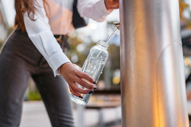 Beautiful young woman filing her water bottle on the drinking fountain in Darling Harbor in Sydney in Australia. Close-up.