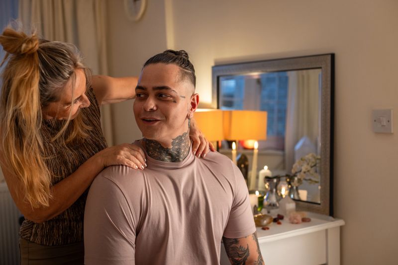 Waist-up shot of a young adult receiving a reiki therapy session from a licensed massage therapist. She is performing an energy healing session on a calm client. The setting exudes warmth and tranquillity with soft lighting, candles, and crystals enhancing the therapeutic ambience. 

Videos of a similar scenario are available,