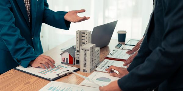 Real estate professionals discuss property models and financial charts during a meeting.