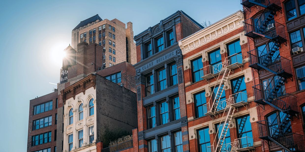 Sunlit urban buildings with fire escapes under a clear blue sky.