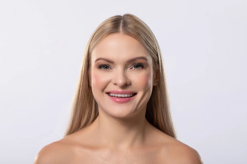 A cheerful woman with long, flowing blonde hair beams with joy, showcasing her natural beauty and confidence radiantly