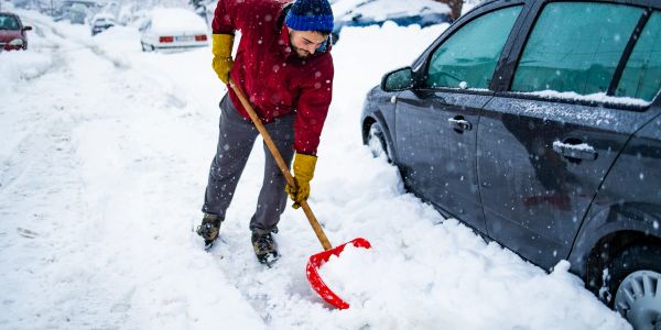 Man shoveling snow next to a car.