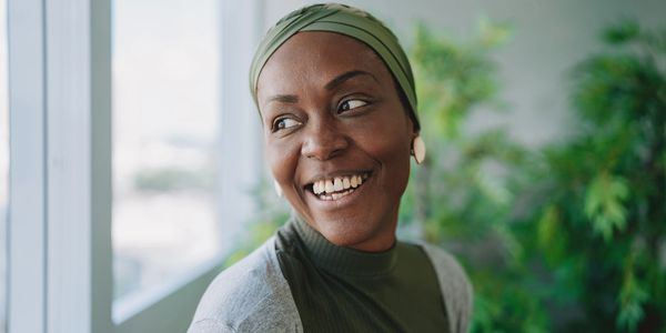 Smiling woman wearing a green headscarf and sweater, looking out a window.