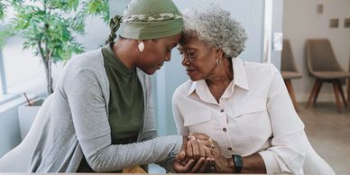 Two women share a tender moment, holding hands and touching foreheads.