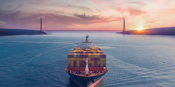 Cargo ship sailing towards a bridge at sunset.