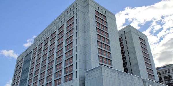 Low-angle view of a tall concrete building with small windows against a blue sky.