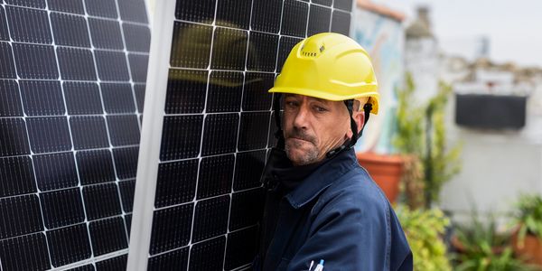 Worker in yellow helmet installing solar panels outdoors.