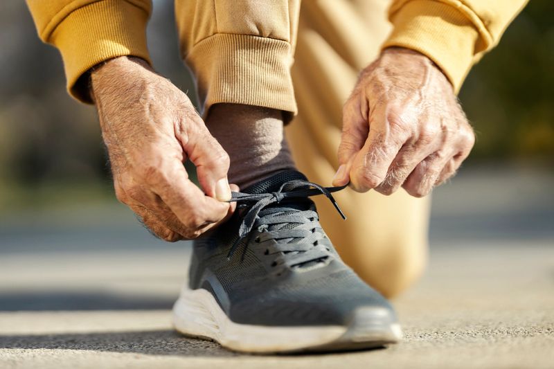 Cropped picture of an unrecognizable senior sportsman tying shoelace on sneaker for outdoor fitness.