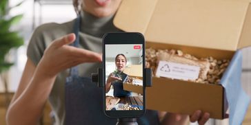 Photo of phone on a tripod filming UGC content with model in the background holding a product.