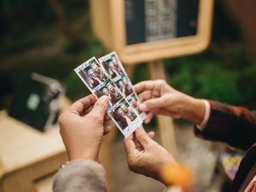 Two people holding photo booth strips with joyful pictures.