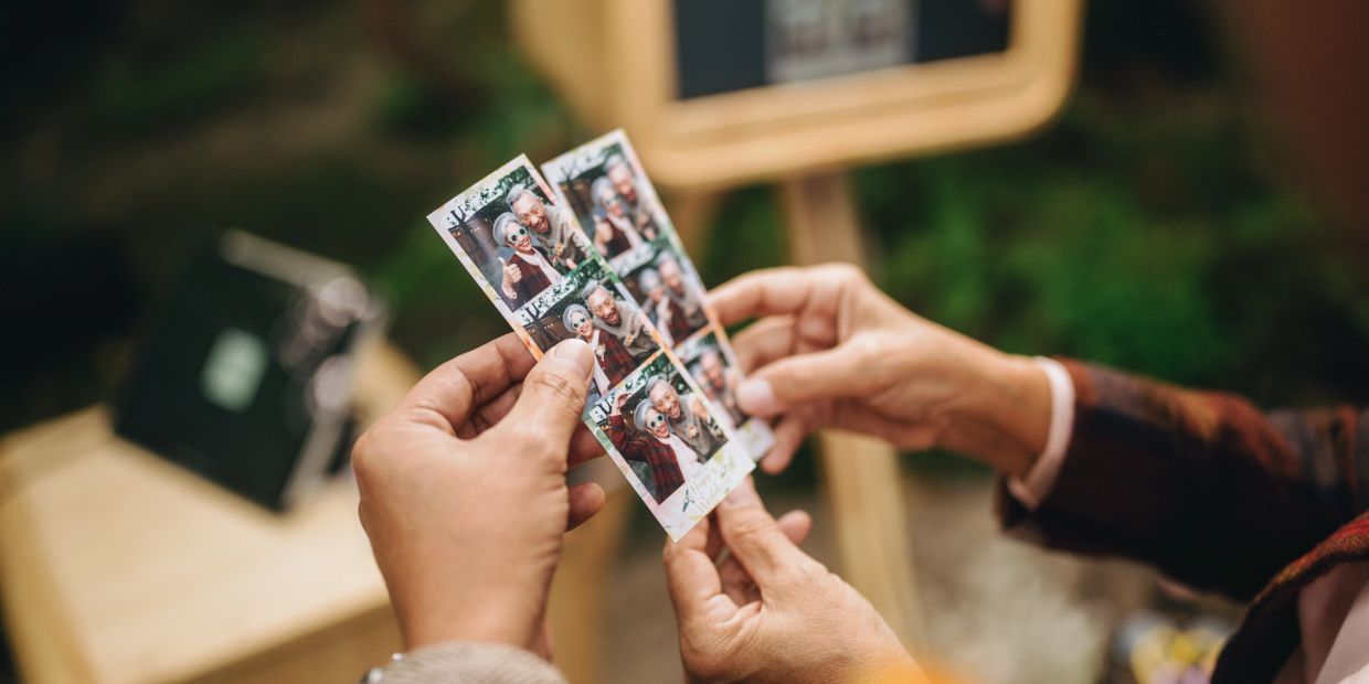 Hands holding photo booth strips with smiling people.
