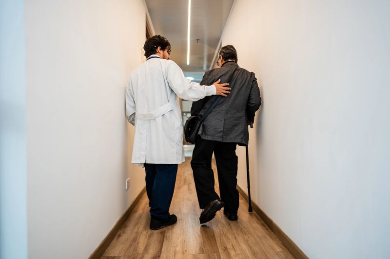 Rear view of a doctor helping patient to walk on a hospital