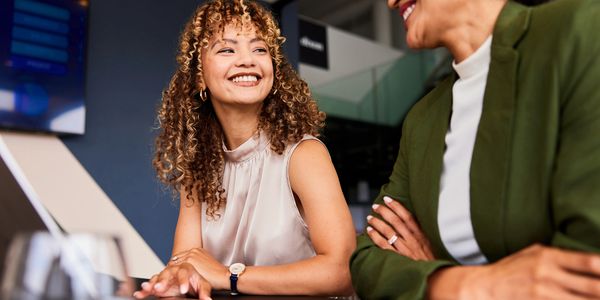 Two women happily discussing work at a laptop in an office.