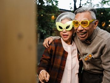 Elderly couple wearing fun yellow novelty glasses, enjoying a joyful moment together.