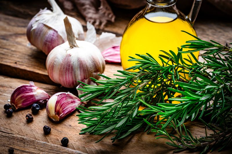 Rosemary, garlic and olive oil on rustic wooden table. High resolution 42Mp studio digital capture taken with SONY A7rII and Zeiss Batis 40mm F2.0 CF lens