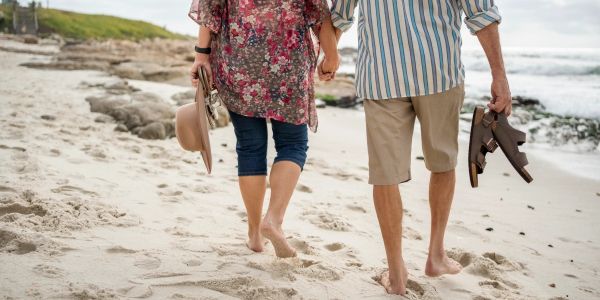 Couple walking barefoot on the beach holding hands.