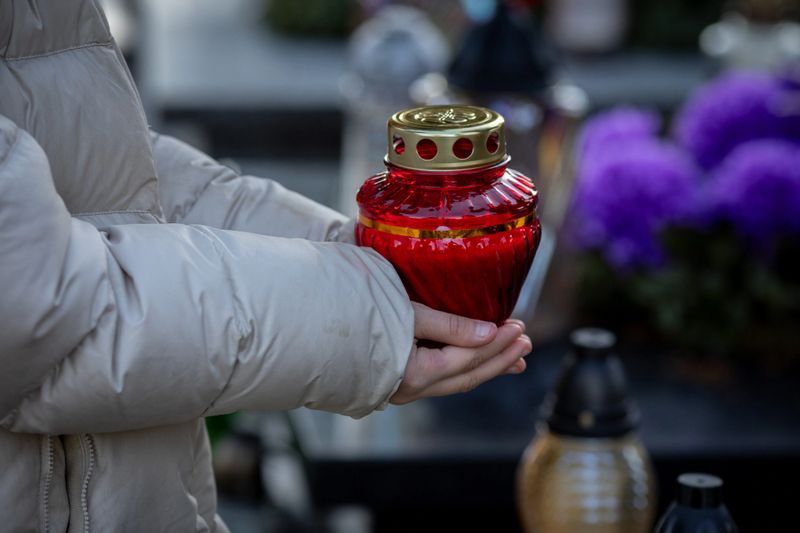 A solemn moment unfolds as a person holds a decorative lantern in a quiet cemetery, reflecting on memories