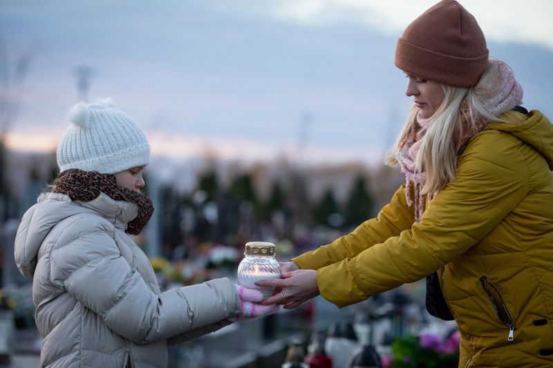 A deeply touching scene depicts a woman and a child holding a glowing lantern at a serene cemetery during sunset