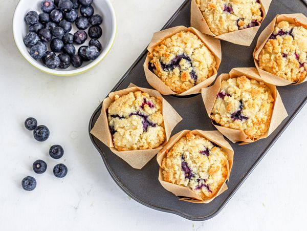 Blueberry muffins in a baking tray with fresh blueberries nearby.