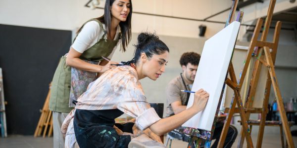 Young woman painting while others watch in art studio.