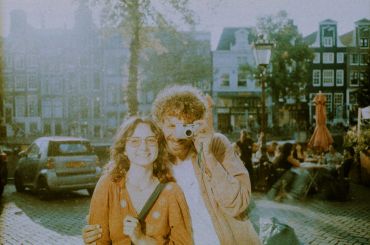 Couple posing with a camera in a sunny town square.