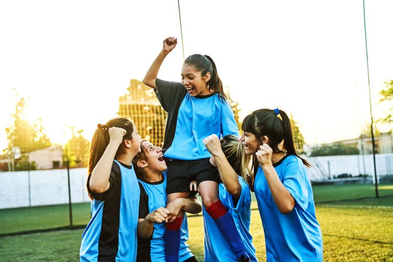 Cheerful girls soccer player carrying a teammate on their shoulders after winning a match. The female soccer team is celebrating their success and enjoying the moment together on the outdoor field.