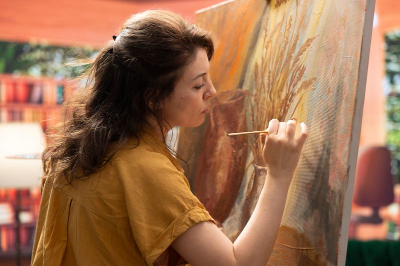 Inspired artist works on a canvas to create a masterpiece in atelier, using bristles to apply dye with precision. Showing her skill during creative process to create unique painting for the gallery.