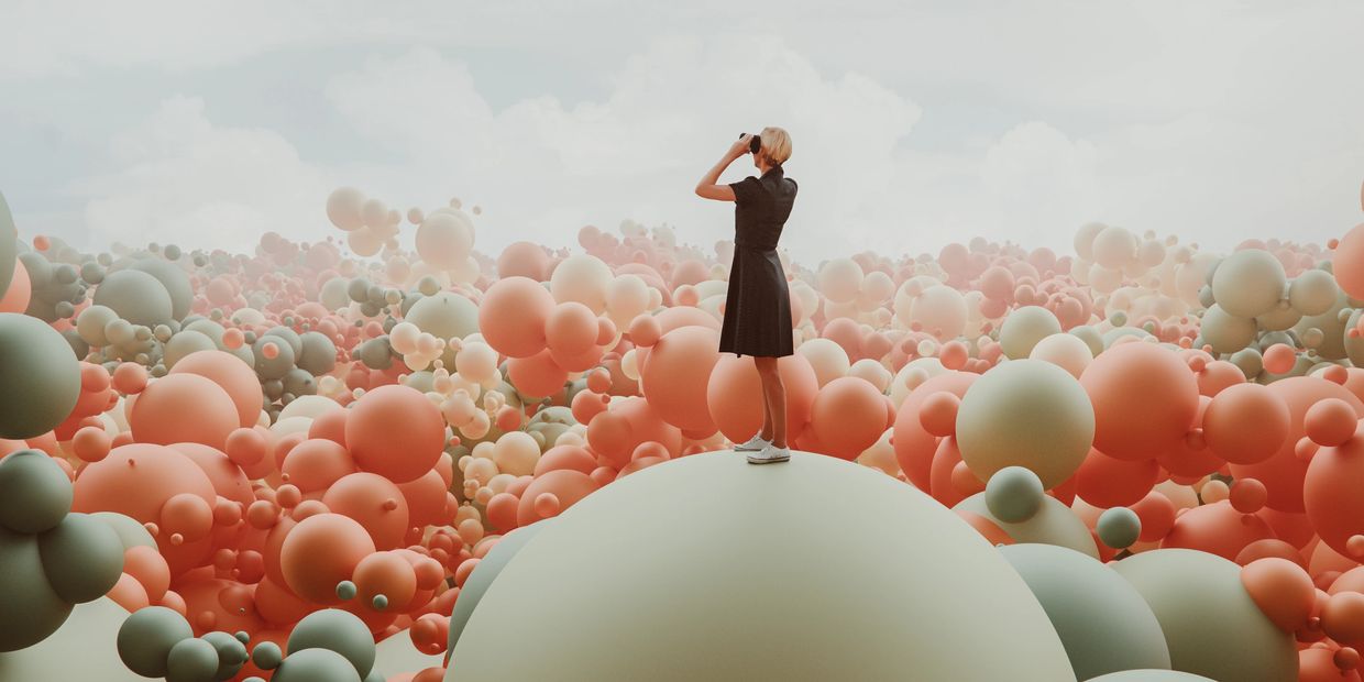 A woman in a black dress stands on a giant sphere surrounded by numerous colorful spheres.