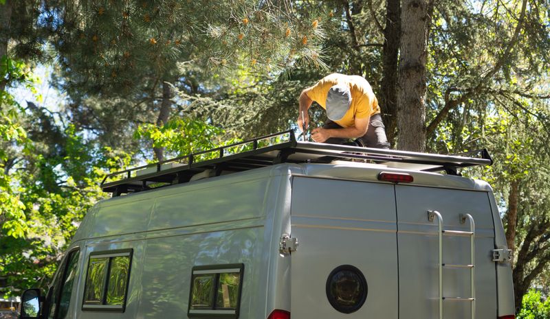 Skilled technician installing a roof rack on a camper van in a forest, preparing for outdoor adventures